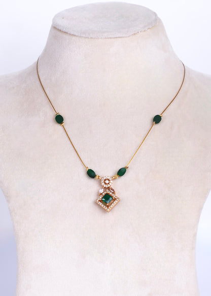 A gold chain necklace with green oval beads and a central diamond-shaped pendant, displayed on a cream-colored mannequin bust.