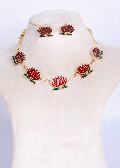 A gold-tone necklace and matching stud earrings set featuring red lotus flowers with green leaves, displayed on a cream-colored jewelry bust.
