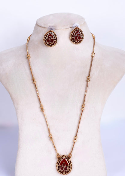 Gold-tone necklace and matching stud earrings with teardrop-shaped red stone inlays, displayed on a cream jewelry bust against a white background.