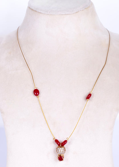 A gold chain necklace with red beads and a central crystal-encrusted pendant, displayed on a cream-colored mannequin bust.