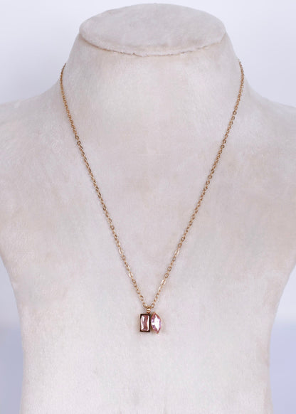 A delicate rose gold chain necklace with a small rectangular pendant featuring a pinkish-red stone, displayed on a cream-colored mannequin bust.