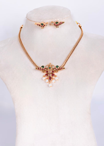 Gold-tone jewelry set displayed on a cream mannequin bust, featuring a necklace with a floral pendant, matching earrings, and a small bracelet, decorated with green and red stones and white faux pearls.