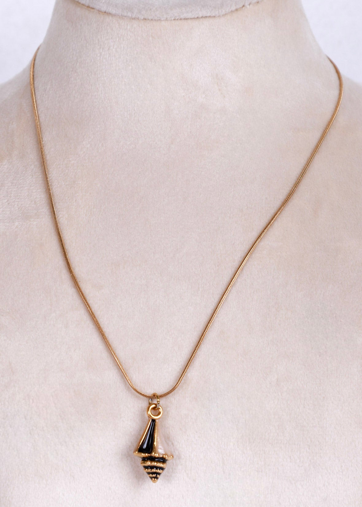 A gold chain necklace with a small gold and black striped pendant, displayed on a cream-colored jewelry bust.