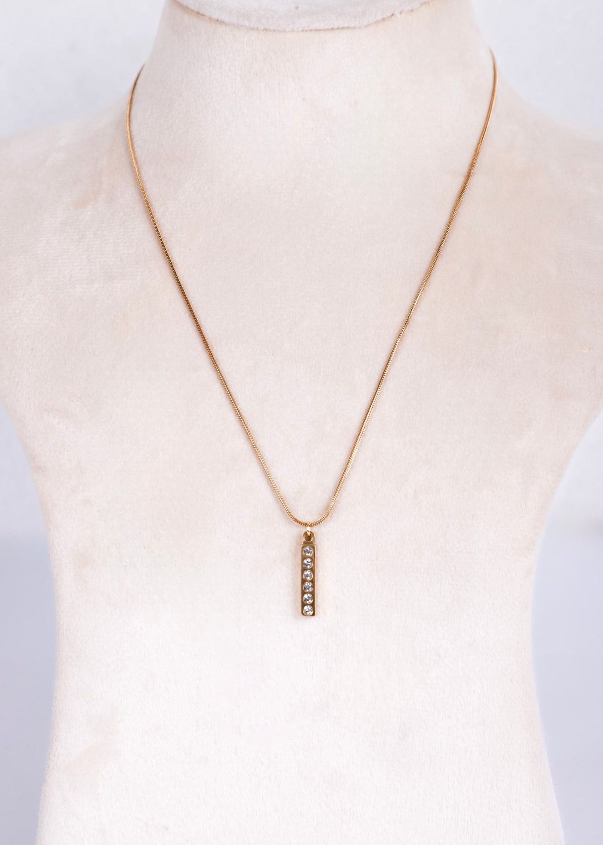 A delicate antish tarnish gold chain necklace with a small vertical bar pendant set with clear stones, displayed on a cream-colored mannequin bust.