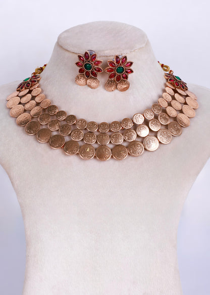 A gold-toned coin necklace set displayed on a cream-colored mannequin bust, featuring a multi-strand coin collar necklace and matching flower-shaped stud earrings with red and green enamel details.