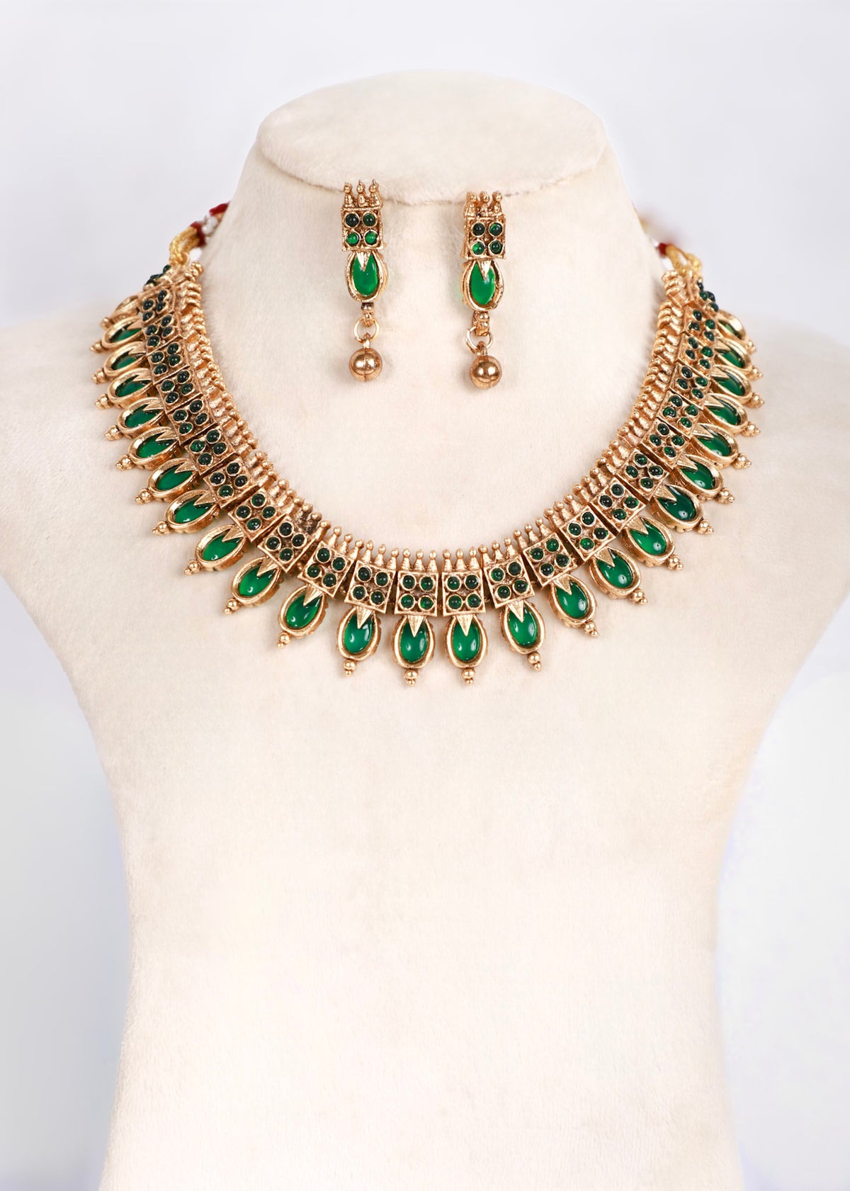 Gold-tone statement necklace and matching drop earrings set with green teardrop-shaped stones, displayed on a cream-colored jewelry bust.