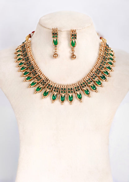 Gold-tone statement necklace and matching drop earrings set with green teardrop-shaped stones, displayed on a cream-colored jewelry bust.