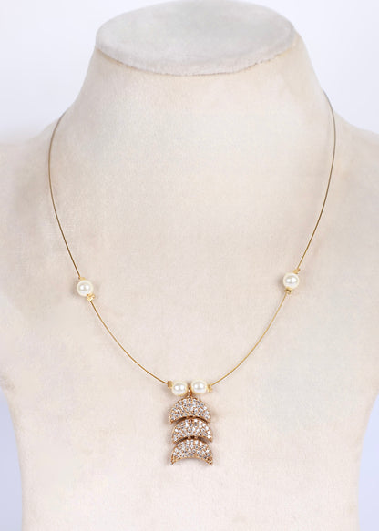 A delicate gold chain necklace displayed on a cream-colored mannequin bust. The necklace features three small white pearl beads spaced along the chain and a central pendant made of stacked, diamond-encrusted crescent moon shapes.