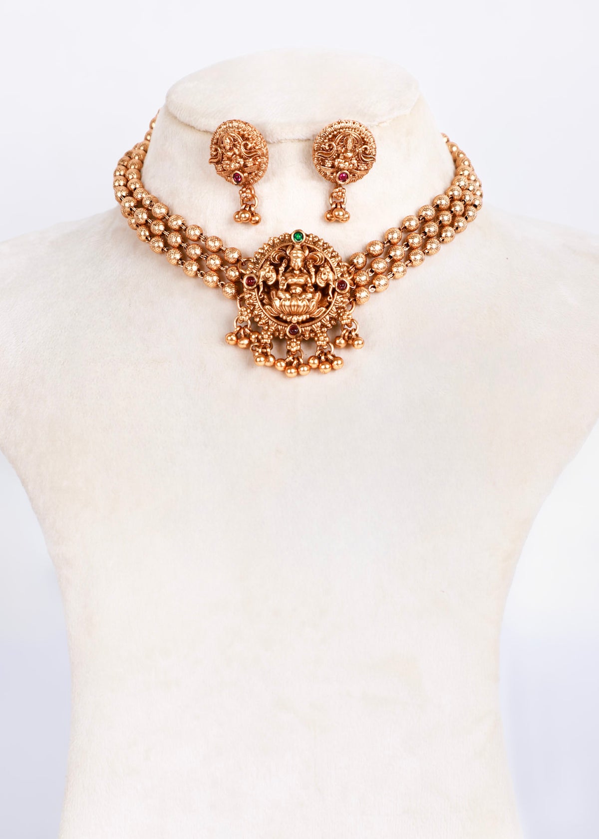 Gold-toned traditional Indian jewelry set featuring a necklace and matching earrings displayed on a cream-colored mannequin bust.