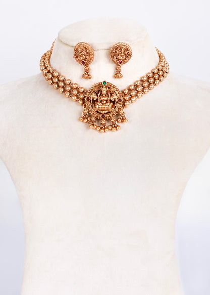 Gold-toned traditional Indian jewelry set featuring a necklace and matching earrings displayed on a cream-colored mannequin bust.