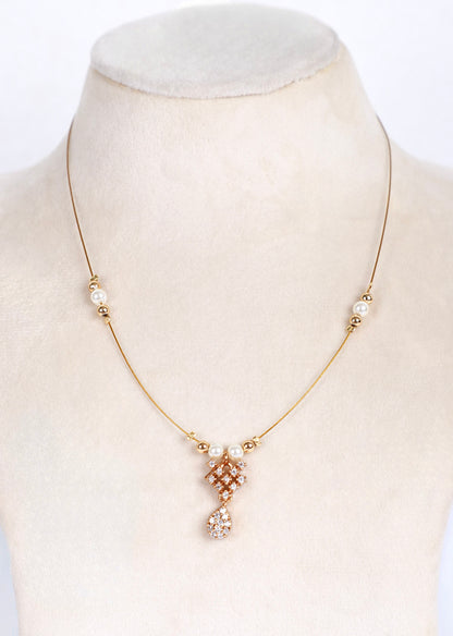 A delicate gold chain necklace displayed on a cream-colored jewelry bust. The necklace features small pearl-like beads spaced along the chain and a central pendant with a gold-toned geometric pattern accented by clear rhinestones and a dangling clear teardrop charm.