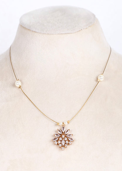A delicate gold chain necklace displayed on a cream-colored mannequin bust. The necklace features small pearl-like beads on either side of the chain and a central gold pendant with clear rhinestones arranged in a floral or snowflake pattern.