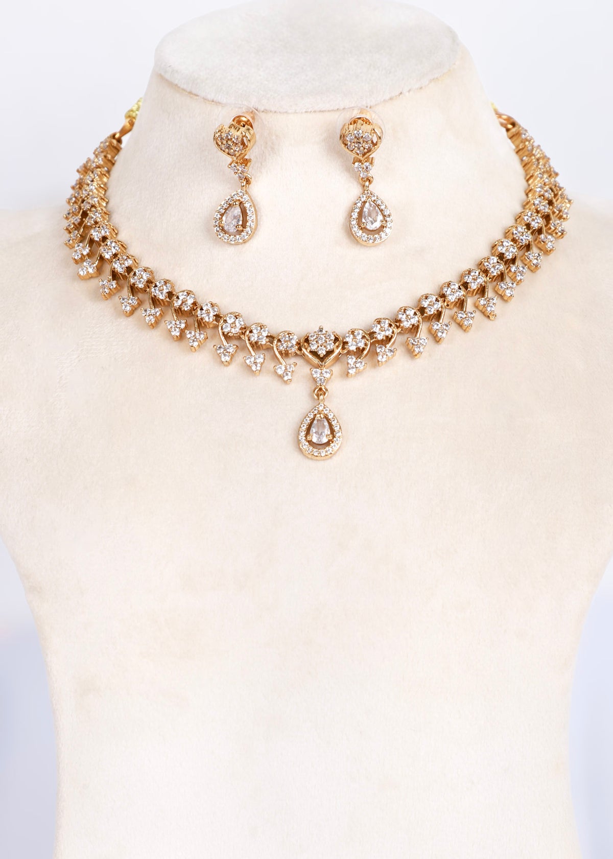 Gold-plated jewelry set featuring a choker necklace and matching drop earrings, both adorned with clear teardrop and round stones, displayed on a cream-colored mannequin bust.