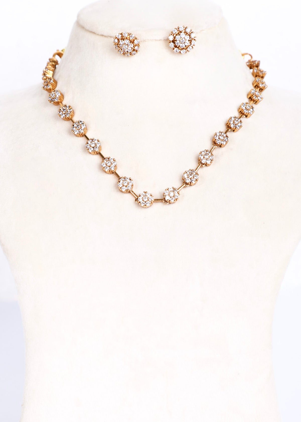 A gold-tone jewelry set displayed on a cream-colored mannequin bust, featuring a floral cluster necklace and matching stud earrings.
