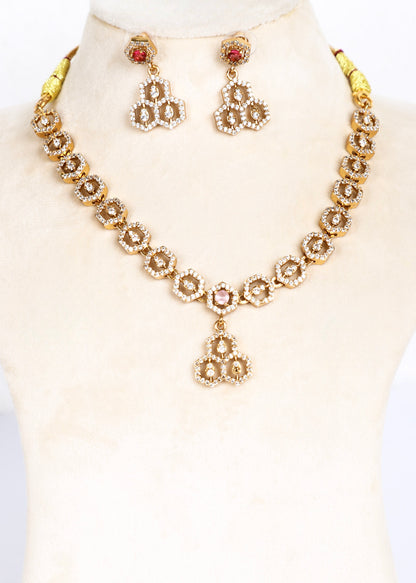 Gold-toned traditional necklace and matching drop earrings displayed on a cream jewelry bust. The floral-style necklace and matching earrings feature clear stones arranged in clusters with small red gemstone accents at the top of each earring.