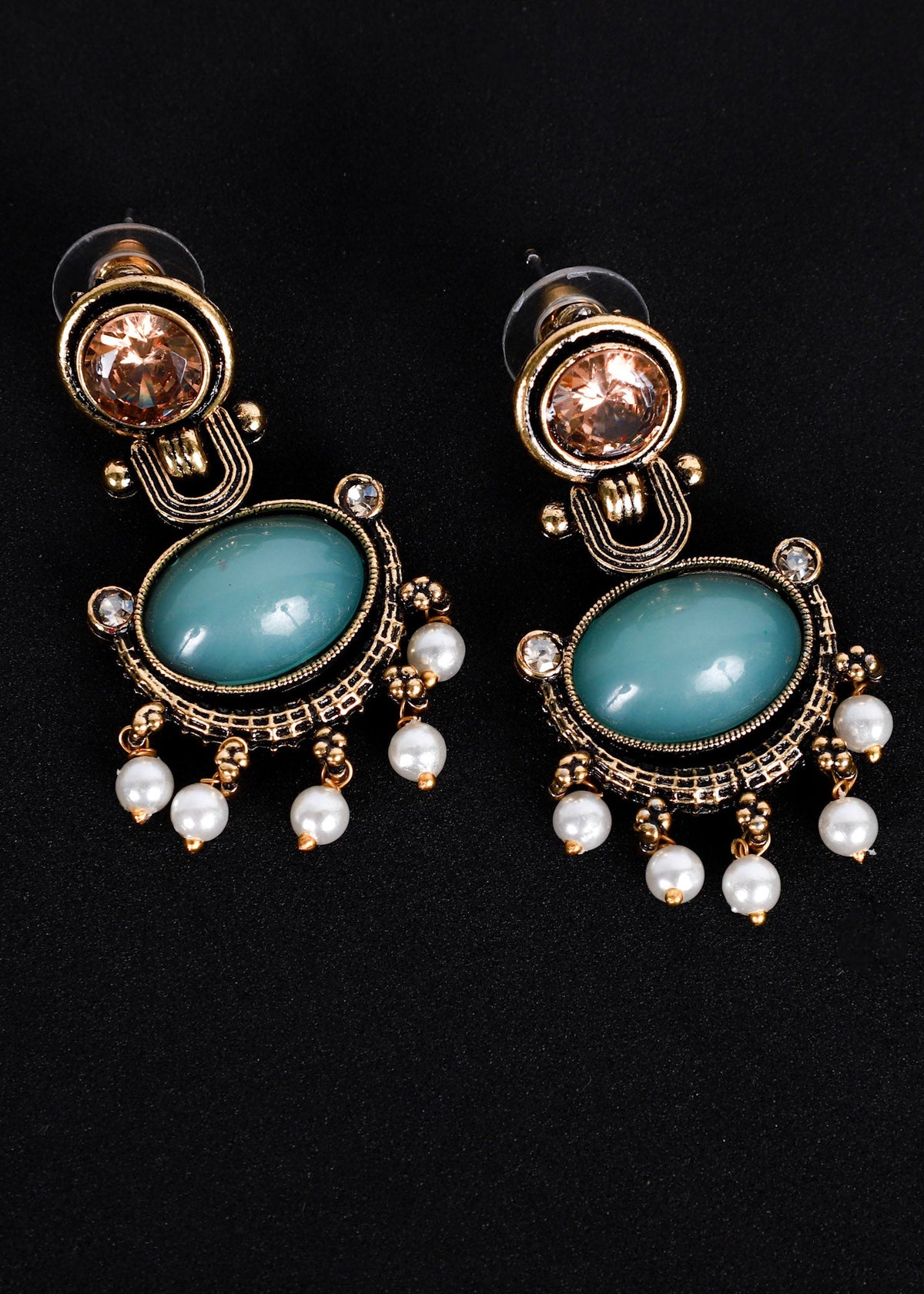 A pair of ornate drop earrings with oval light blue stones, gold-toned filigree detailing, and dangling white faux pearls, displayed on a black background.