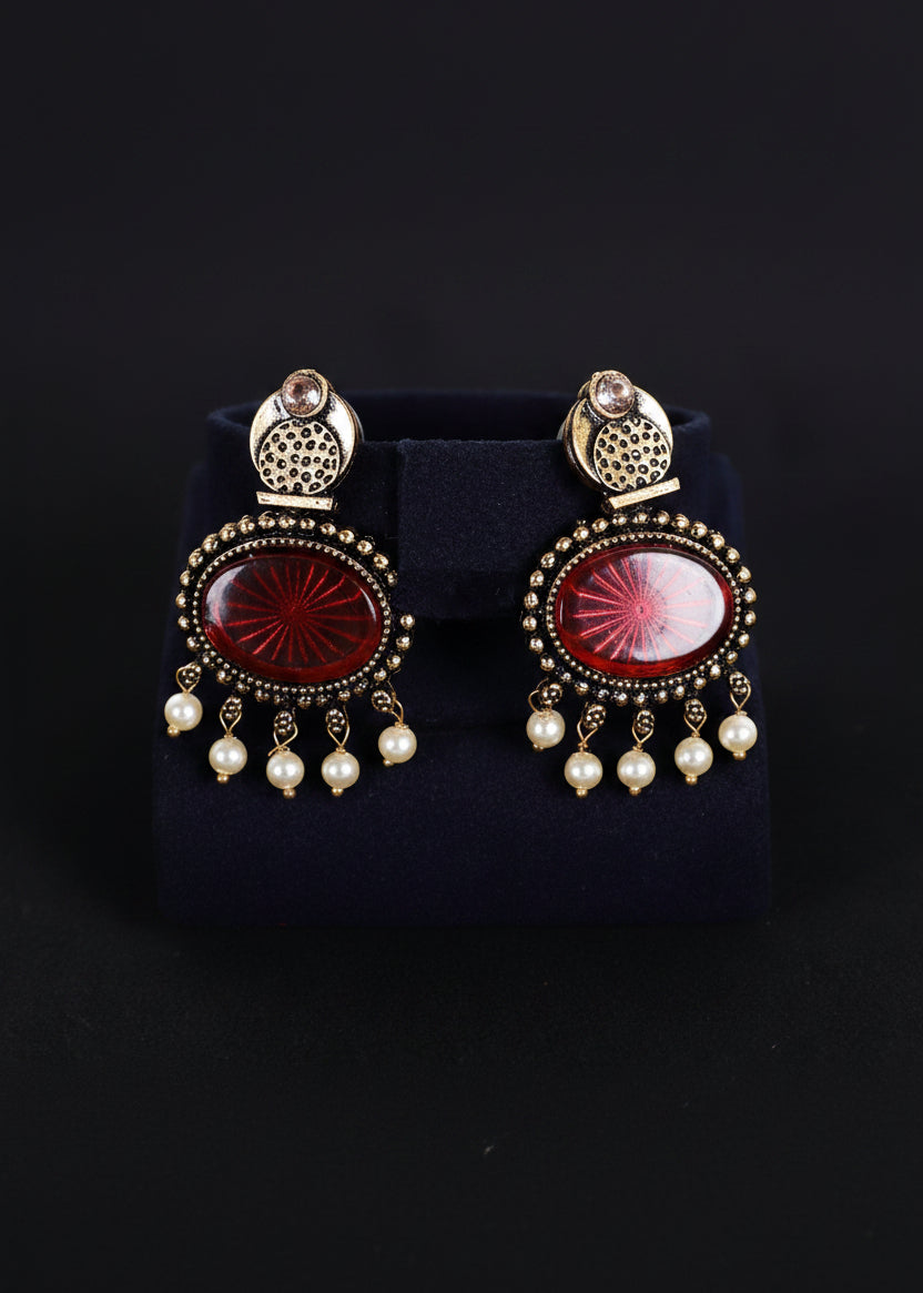 A pair of ornate gold-toned statement earrings with oval red cabochon stones and dangling white pearl beads, 