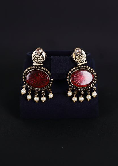 A pair of ornate gold-toned statement earrings with oval red cabochon stones and dangling white pearl beads, 