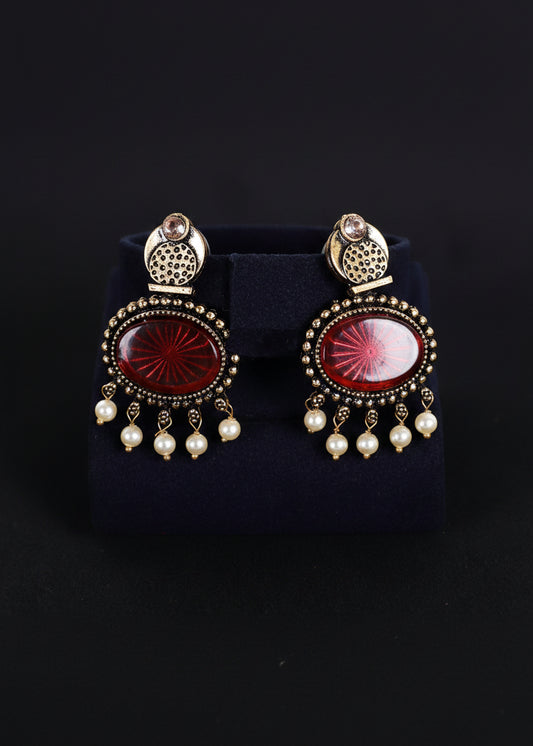 A pair of ornate gold-toned statement earrings with oval red cabochon stones and dangling white pearl beads, 