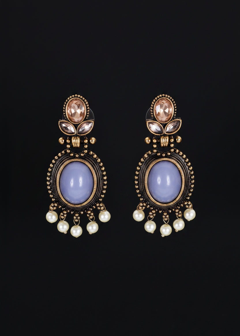 A pair of ornate drop earrings. Each earring features a large oval pale lavender stone surrounded by gold-toned beaded detailing, with small white pearl-like drops below and a small peach stone near the top.