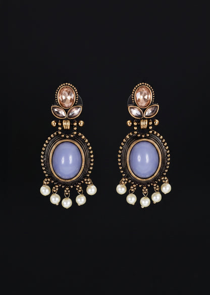 A pair of ornate drop earrings. Each earring features a large oval pale lavender stone surrounded by gold-toned beaded detailing, with small white pearl-like drops below and a small peach stone near the top.