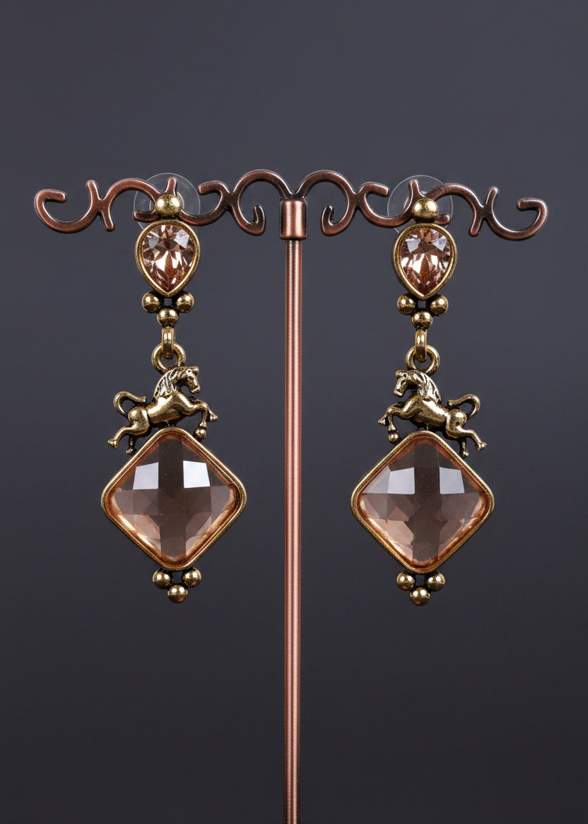 A pair of antique-style drop earrings. The earrings feature oval rose-gold-toned bezel-set stones, small horse charms, and large diamond-shaped pale pink faceted beads.