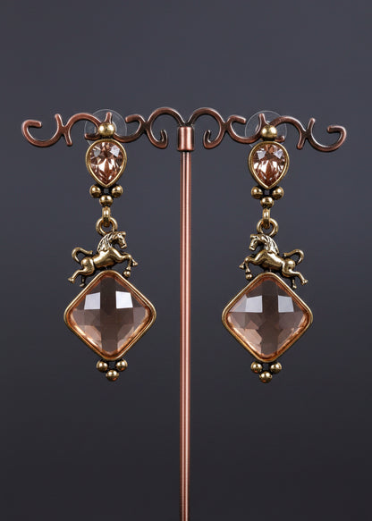 A pair of antique-style drop earrings. The earrings feature oval rose-gold-toned bezel-set stones, small horse charms, and large diamond-shaped pale pink faceted beads.