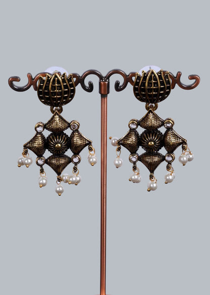 A pair of ornate bronze-toned dangle earrings. The earrings feature textured metallic floral and geometric motifs with small clear rhinestones and dangling white pearl beads.
