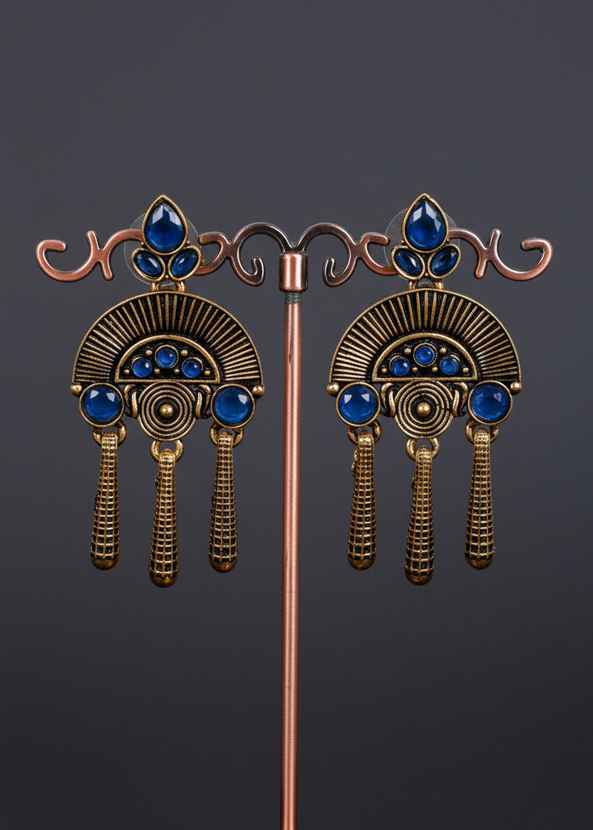 A pair of ornate antique-style drop earrings. The earrings feature a bronze-toned fan-shaped design with blue gemstone accents and three dangling textured tassels.