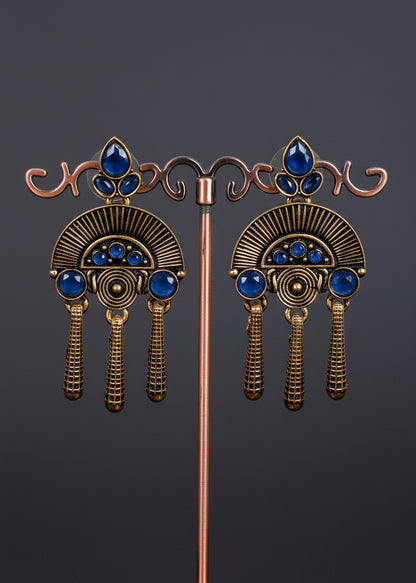 A pair of ornate antique-style drop earrings. The earrings feature a bronze-toned fan-shaped design with blue gemstone accents and three dangling textured tassels.