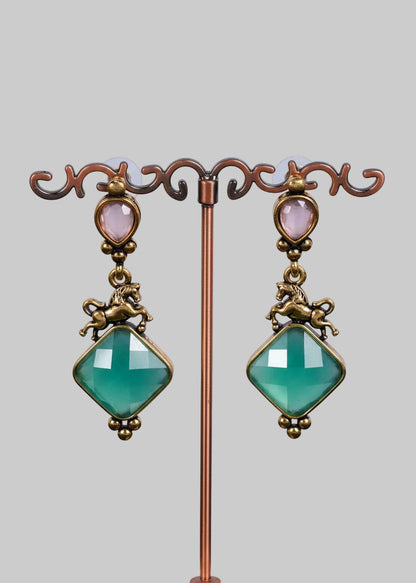 A pair of antique-style drop earrings. Each earring features a faceted light green diamond-shaped gemstone, an antique bronze horse figure, a small oval pale pink stone, and a matching horse connector.