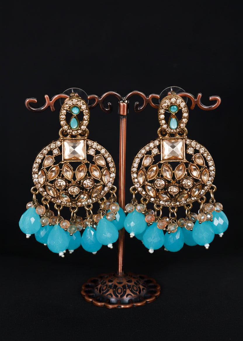 A pair of ornate gold-toned Indian chandbali earrings with turquoise blue bead drops and clear rhinestone embellishments.