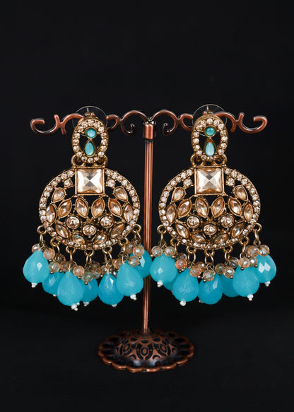 A pair of ornate gold-toned Indian chandbali earrings with turquoise blue bead drops and clear rhinestone embellishments.