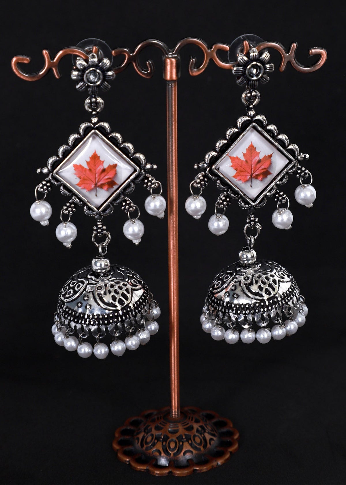 A pair of silver-toned traditional Indian jhumka earrings with white pearl bead drops and a central white square inlay featuring a red maple leaf.