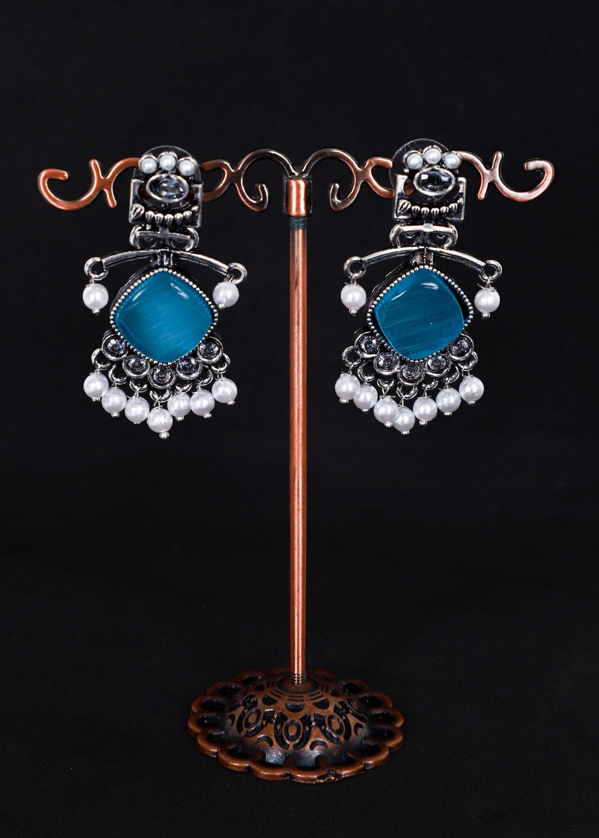 A pair of silver-toned statement earrings with aqua blue gemstone centers and white pearl bead drops.
