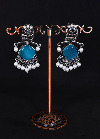A pair of silver-toned statement earrings with aqua blue gemstone centers and white pearl bead drops.