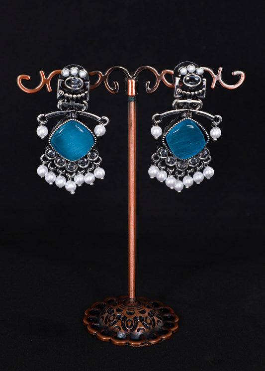 A pair of silver-toned statement earrings with aqua blue gemstone centers and white pearl bead drops.