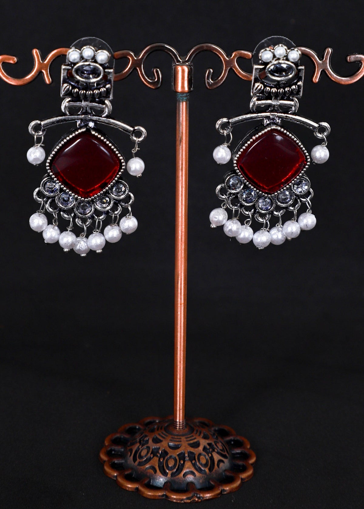 A pair of ornate silver-toned dangle earrings with large deep red square stones and rows of white pearl-like beads.