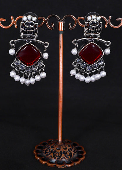 A pair of ornate silver-toned dangle earrings with large deep red square stones and rows of white pearl-like beads.