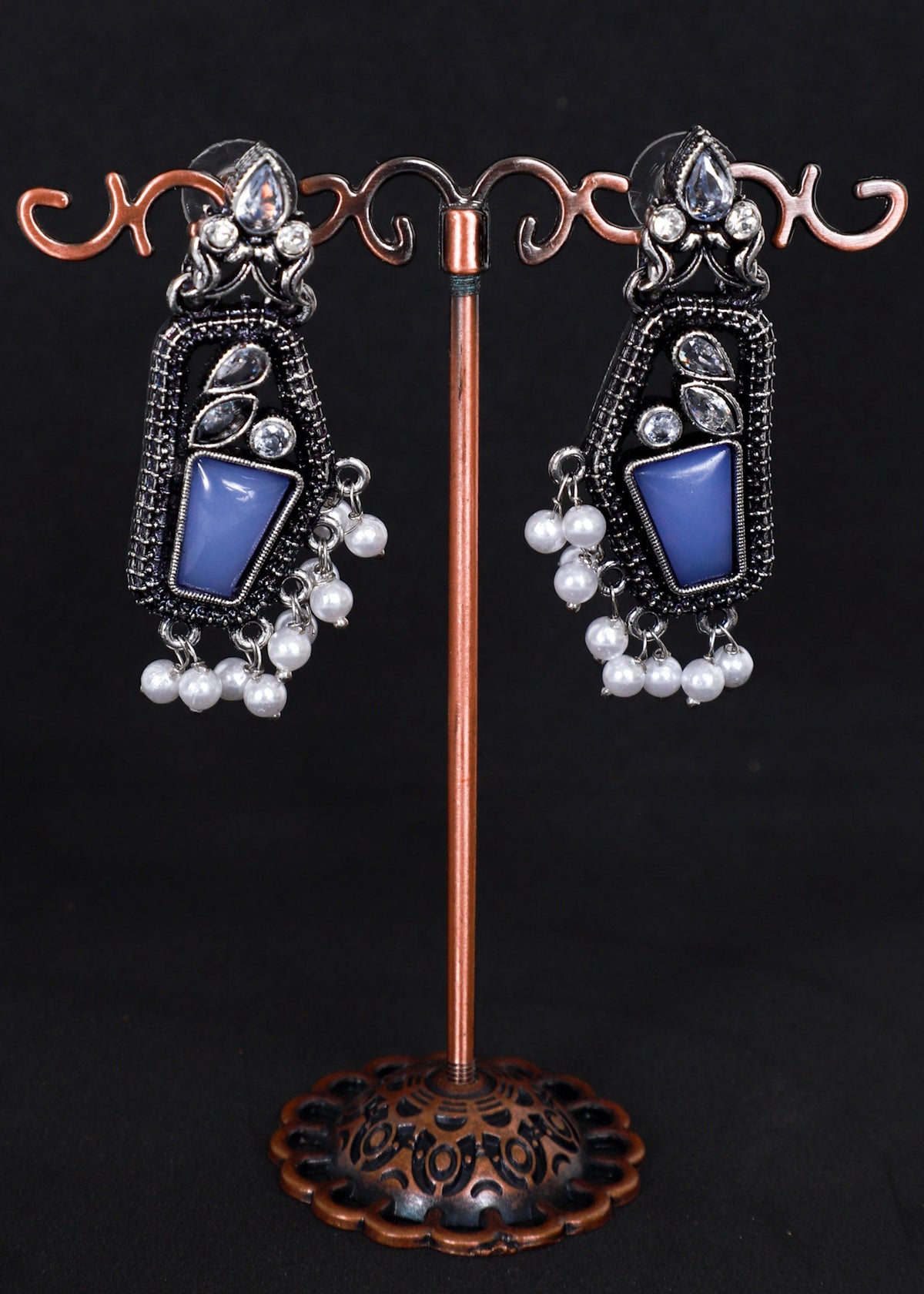 A pair of ornate silver-toned dangle earrings with blue rectangular stones and white pearl-like drops.