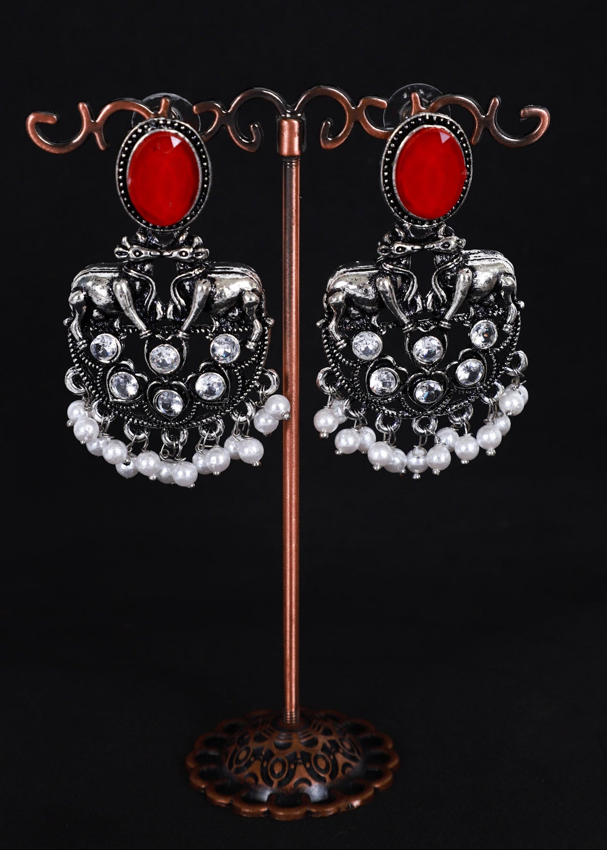 A pair of ornate silver-toned dangle earrings with oval red stones and white pearl-like drops.