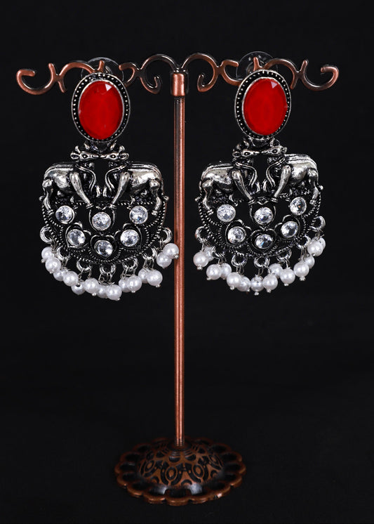 A pair of ornate silver-toned dangle earrings with oval red stones and white pearl-like drops.