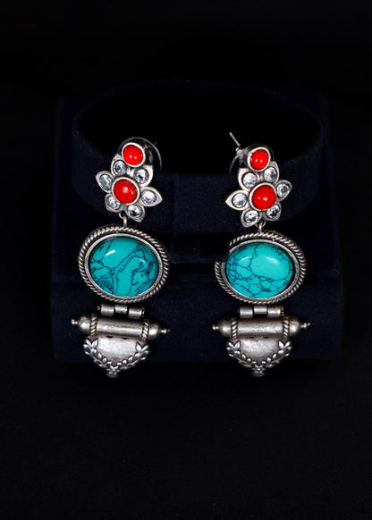 A pair of silver-toned dangle earrings. Each earring features a silver floral stud with three round orange-red stones, a round turquoise-blue stone in a silver bezel, and a dangling silver bell-shaped charm.
