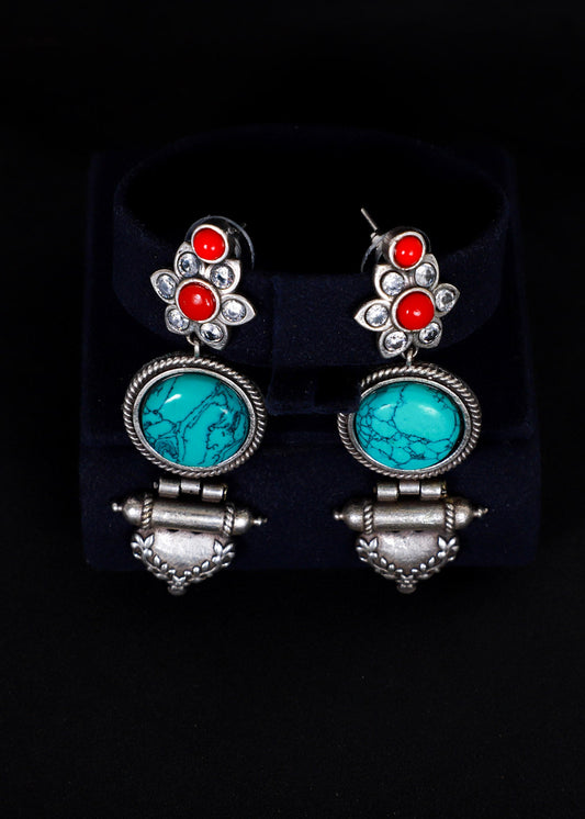 A pair of silver-toned dangle earrings. Each earring features a silver floral stud with three round orange-red stones, a round turquoise-blue stone in a silver bezel, and a dangling silver bell-shaped charm.