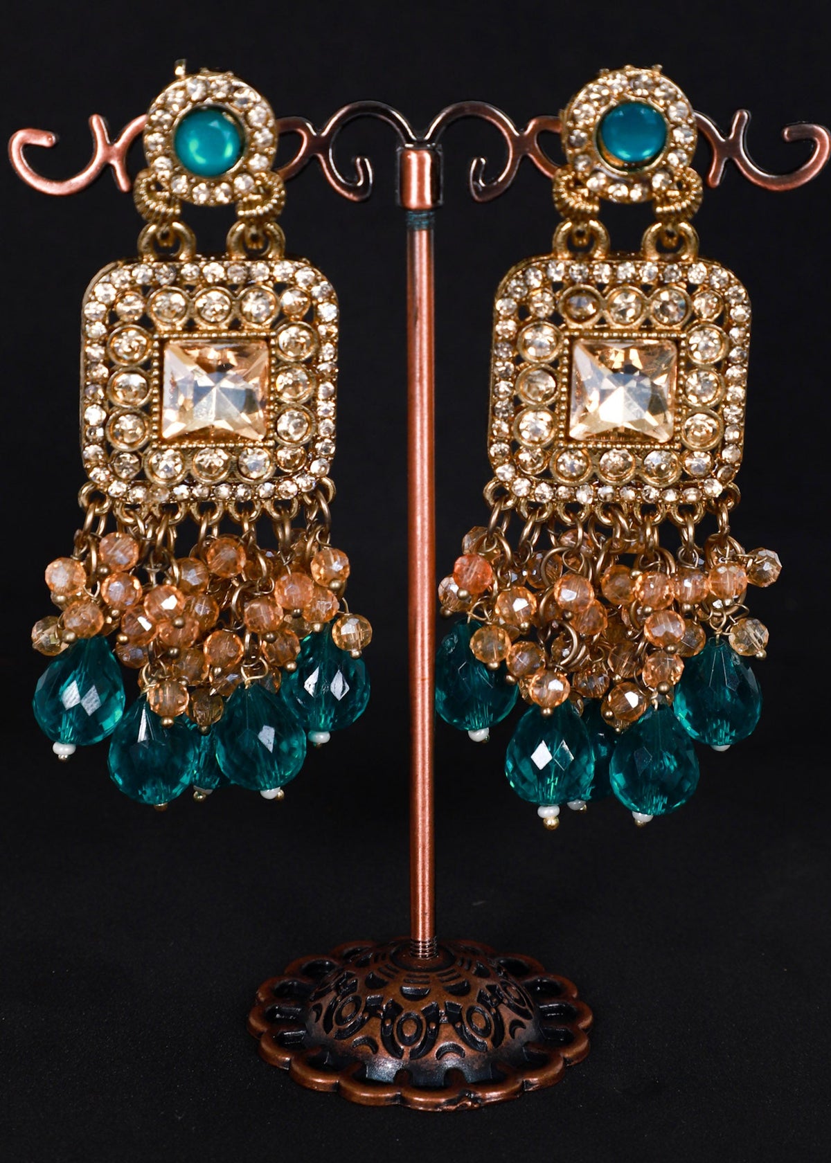 A pair of ornate gold-toned dangle earrings. The earrings feature turquoise blue faceted beads, clear rhinestones, and peach-colored pearl-like accents.