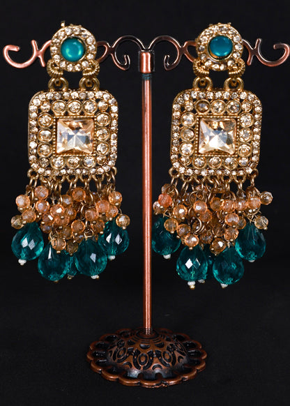 A pair of ornate gold-toned dangle earrings. The earrings feature turquoise blue faceted beads, clear rhinestones, and peach-colored pearl-like accents.