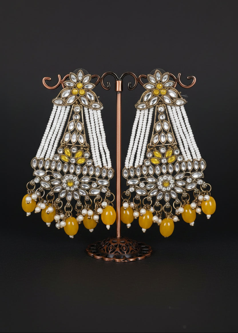 A pair of ornate Indian chandbali earrings. The earrings feature silver-toned metalwork, white beaded strands, yellow gemstone accents, and dangling yellow beads.