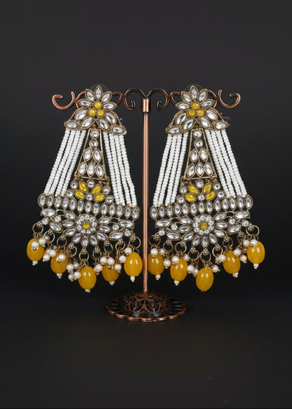 A pair of ornate Indian chandbali earrings. The earrings feature silver-toned metalwork, white beaded strands, yellow gemstone accents, and dangling yellow beads.