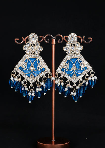 A pair of ornate blue and silver chandelier earrings. The earrings feature a silver-toned filigree frame set with clear rhinestones, a vibrant blue enamel center, and dangling blue crystal beads and pearl accents.