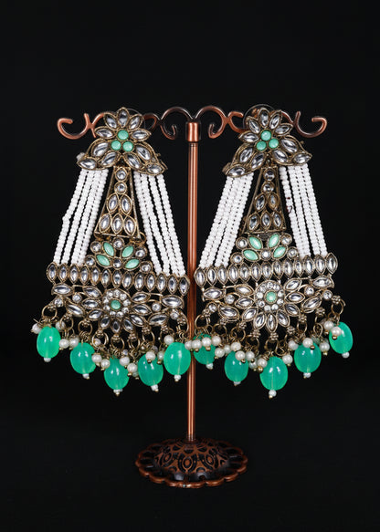 A pair of ornate Indian chandbali earrings. The earrings feature silver-toned metalwork, white bead strands, and green stone accents.